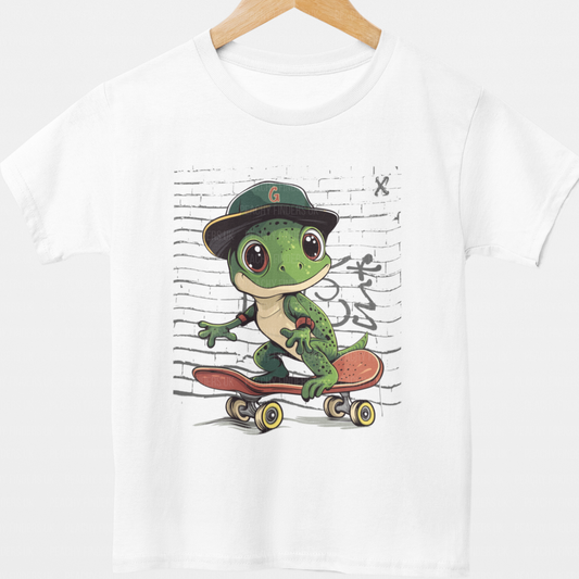 Kids white t-shirt featuring a cool cartoon gecko skateboarding in front of a graffiti wall, wearing a cap and elbow pads.