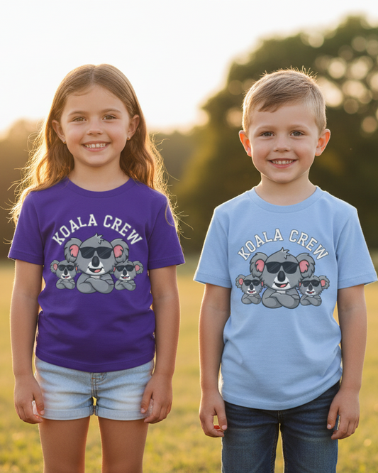 Young girl in purple Koala Crew T-shirt and boy in light blue Koala Crew T-shirt standing outdoors in park