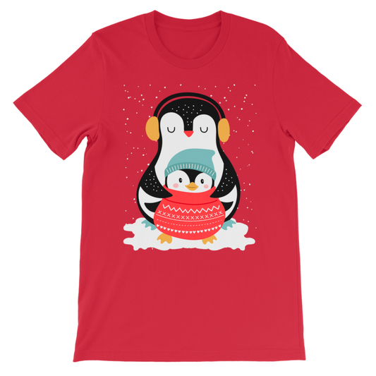 A kids red short-sleeve crewneck t-shirt featuring a cartoon graphic of two penguins hugging under falling snow. The adult penguin wears yellow earmuffs, and the smaller penguin wears a teal knit hat and a red knit sweater.