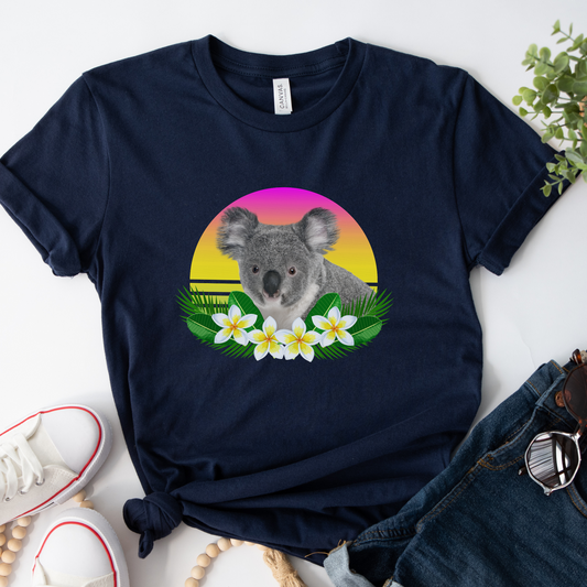 A navy blue t-shirt featuring a graphic of a koala nestled among white and yellow tropical flowers against a vibrant sunset-style background.