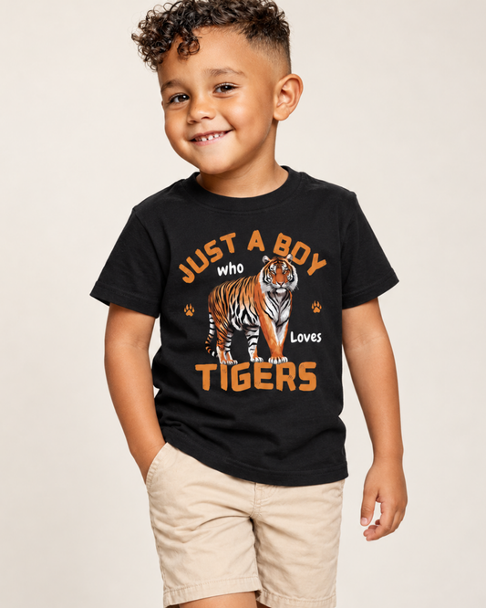 A young boy wearing a black graphic t-shirt with an orange and white tiger design and the text 'JUST A BOY who Loves TIGERS', paired with khaki shorts, against a plain light beige background.