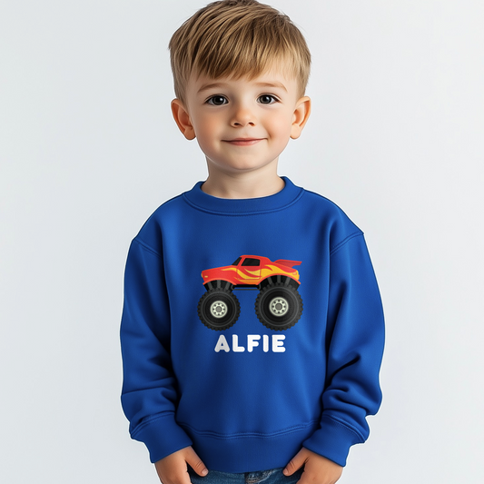 Young boy models a royal blue kids sweatshirt featuring a red and yellow monster truck graphic with large tyres and personalised with the name “Alfiel” printed below the design.