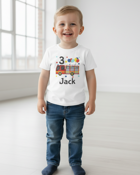 Little boy modelling white personalised 3rd birthday fire truck T-shirt with name “Jack”, bright studio background, graphic fully visible.