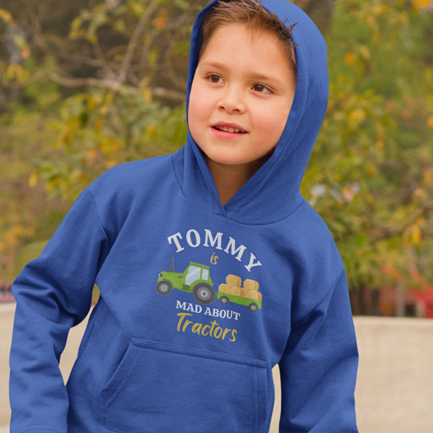Young boy models a royal blue hoodie with personalised name  "TOMMY" is  Mad About Tractors” slogan and green tractor with hay bales on the front.