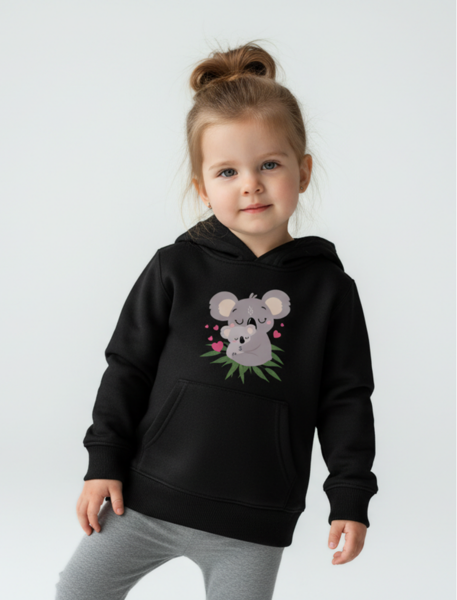 Young girl model wearing a black kids hoodie with cute mum and baby koala graphic, styled with grey leggings in a studio setting
