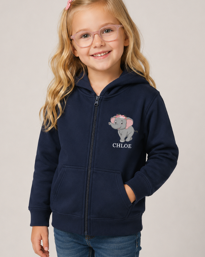 A young girl with blonde hair and glasses wearing a navy blue zip-up hoodie with a cartoon elephant graphic and the name 'CHLOE' printed on the chest, paired with blue jeans, against a plain light grey background.