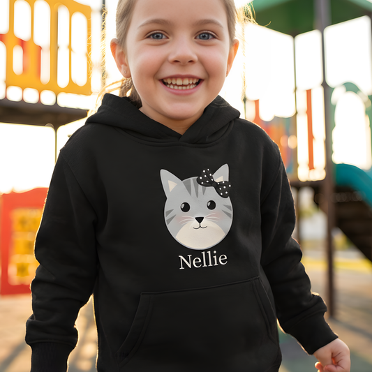 Little girl wearing a black hoodie with a cat graphic and 'Nellie' text on a playground background