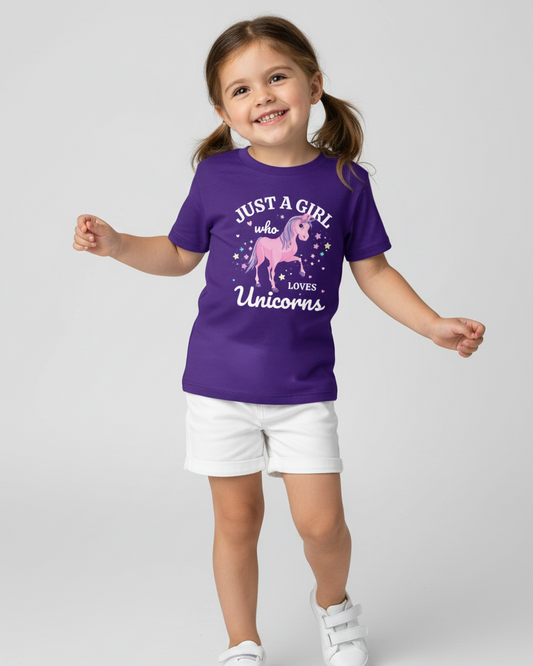 Young girl standing and smiling while wearing a purple “Just a Girl Who Loves Unicorns” t-shirt with a pink unicorn graphic, paired with white shorts and white trainers on a light studio background.