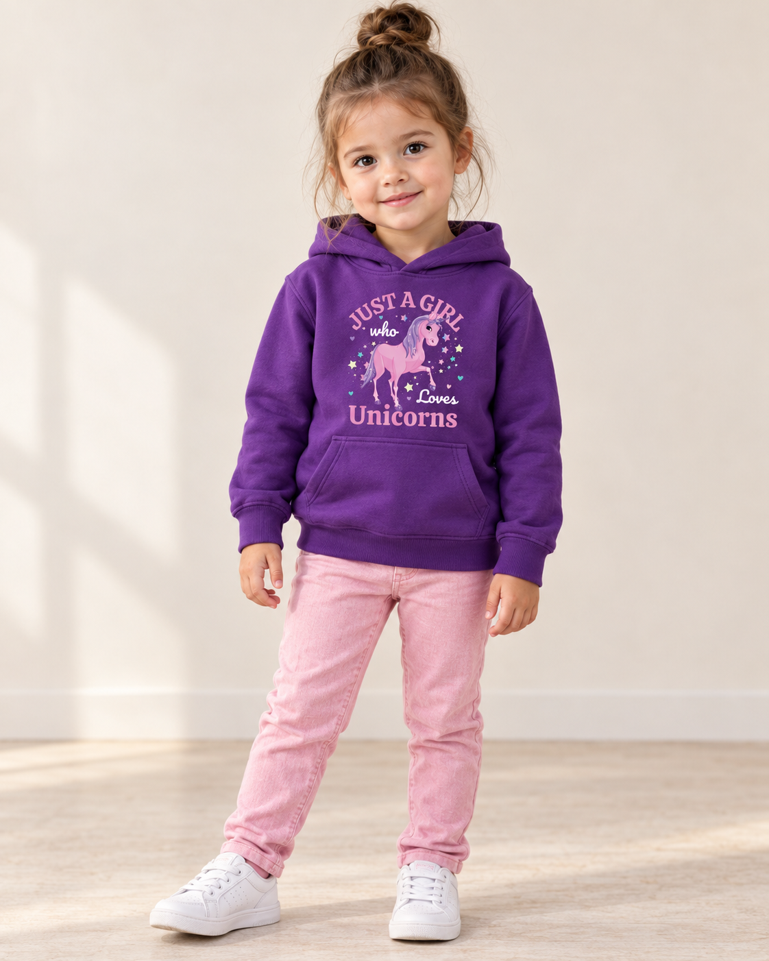 Three-year-old girl wearing a purple “Just a Girl Who Loves Unicorns” hoodie with pink jeans and white trainers.