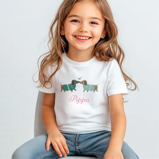 Girl white t-shirt with custom name "Sophie" featuring two cute dachshunds in green jumpers kissing, with pastel heart details.