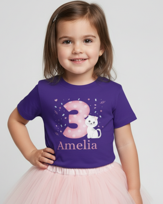 Little girl wearing a personalised purple 3rd birthday t-shirt with pink number 3 and white kitten design, name Amelia printed underneath, styled with a soft pink tutu skirt on a light studio background