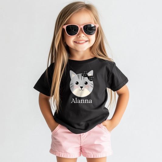 Smiling girl wearing personalised black cat T-shirt with custom name ‘Alanna’ printed beneath a grey kitten face and black polka-dot bow