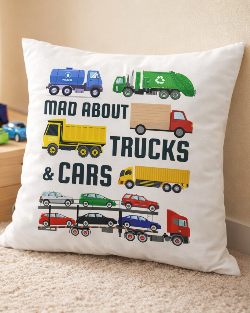 Kids decorative cushion with “Mad About Trucks & Cars” design featuring colourful cartoon trucks and cars, styled in a child’s bedroom floor with toy vehicles in the background.