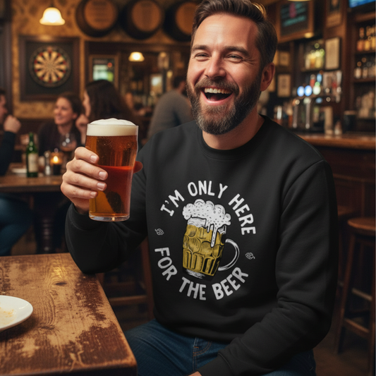 Smiling man in a pub holding a pint of beer while wearing a black “I’m Only Here for the Beer” slogan sweatshirt