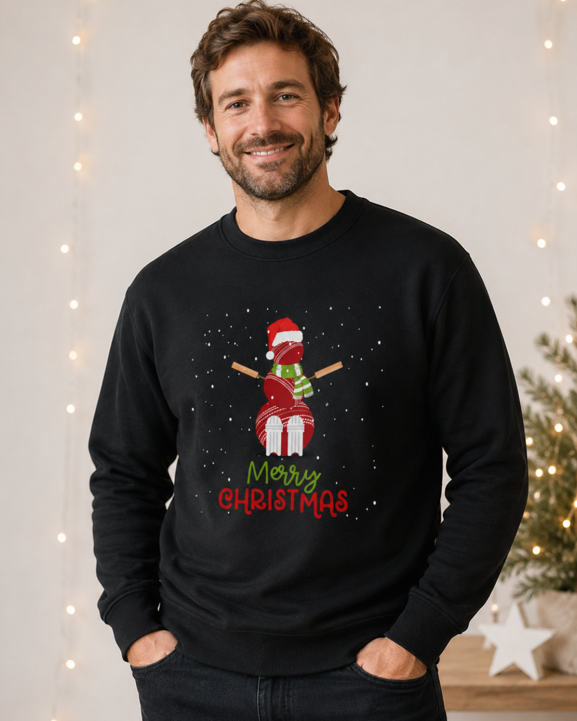 A man wearing a black crewneck sweatshirt with a festive cricket ball snowman with bats for arms, Santa hat and scarf, with 'Merry Christmas' written below. The background features warm string lights and a decorated Christmas tree.