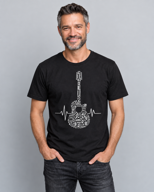 Smiling man wearing a black musical-note guitar and heartbeat T-shirt with dark jeans, hands in his pockets against a light studio background.