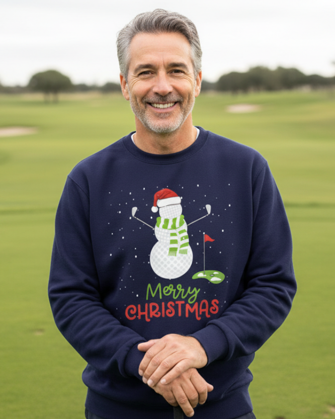 Man wearing a navy Christmas sweatshirt featuring a golf-ball snowman, golf clubs and Merry Christmas lettering while standing on a golf course.