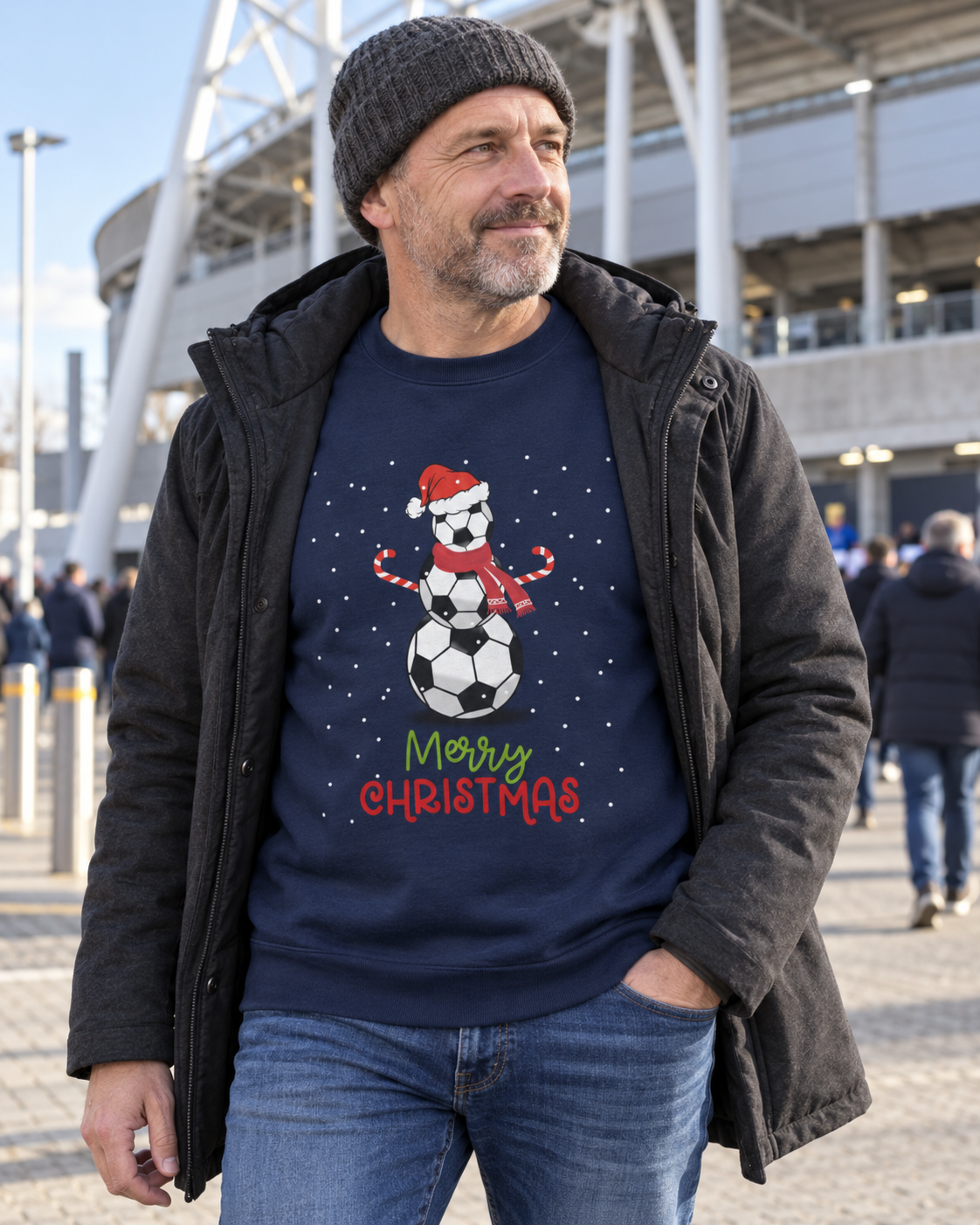 48-year-old man outside a football stadium wearing a navy Football Snowman Christmas jumper, winter coat and grey beanie