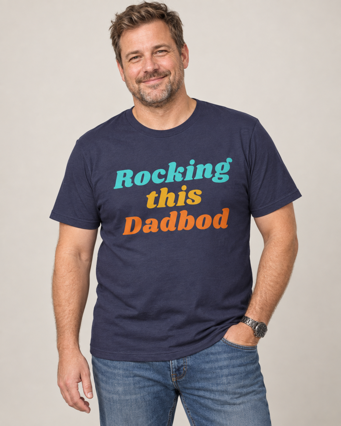 Smiling man with a dad bod wearing a navy Rocking This Dadbod graphic T-shirt with colourful retro lettering.