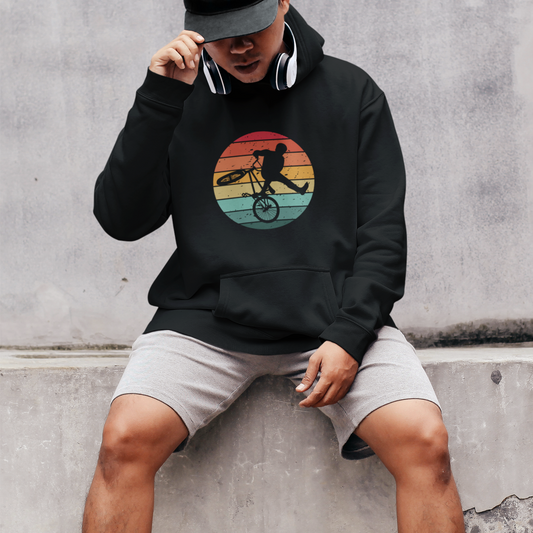Man wearing a black pullover hoodie with retro sunset circle and BMX rider silhouette performing a trick