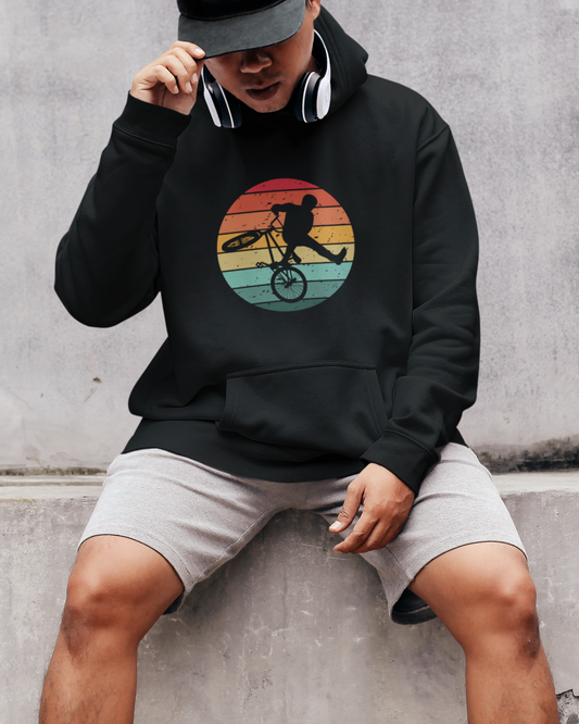 Man wearing a black pullover hoodie with retro sunset circle and BMX rider silhouette performing a trick