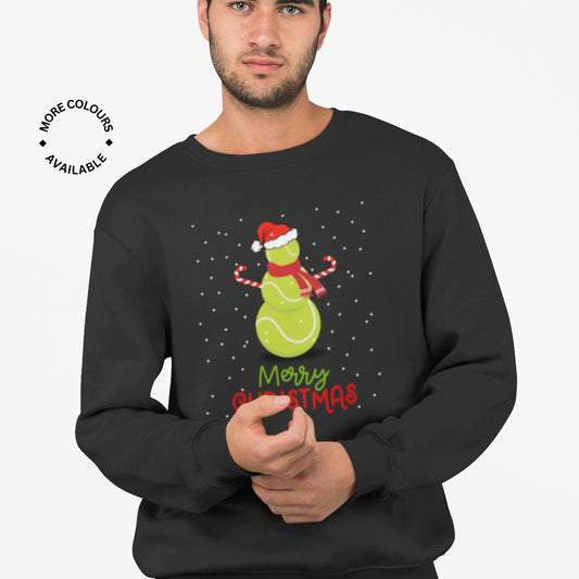 Man wearing a black Christmas sweatshirt featuring a festive green tennis ball snowman design with candy canes and Santa hat, standing in falling snow.