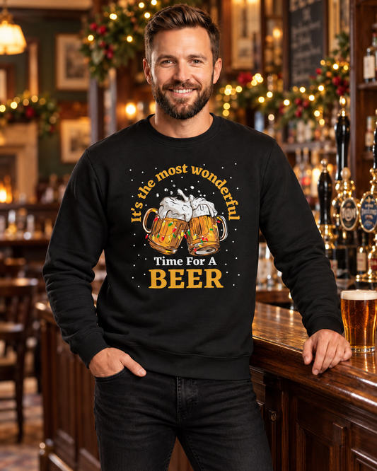A man wearing a black crewneck sweatshirt with a graphic of two clinking beer mugs and the text 'It's the most wonderful Time For A BEER' in a warm, decorated pub setting.