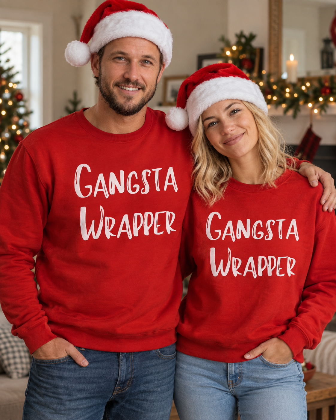 A man and a woman wearing matching red crewneck sweatshirts with the words 'GANGSTA WRAPPER' in white script, each wearing a Santa hat in a cozy holiday living room setting.