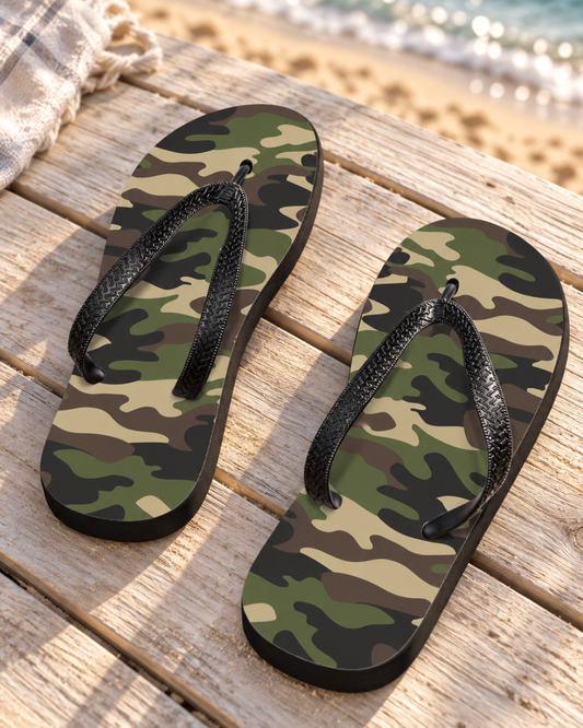 Men’s camouflage flip-flops with black straps and soles on sunlit wooden decking beside the beach.
