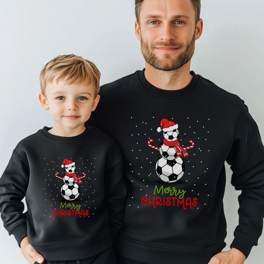 Father and son wearing matching black Christmas sweatshirts featuring a snowman made of footballs with a Santa hat and candy cane arms, perfect for festive football fans.