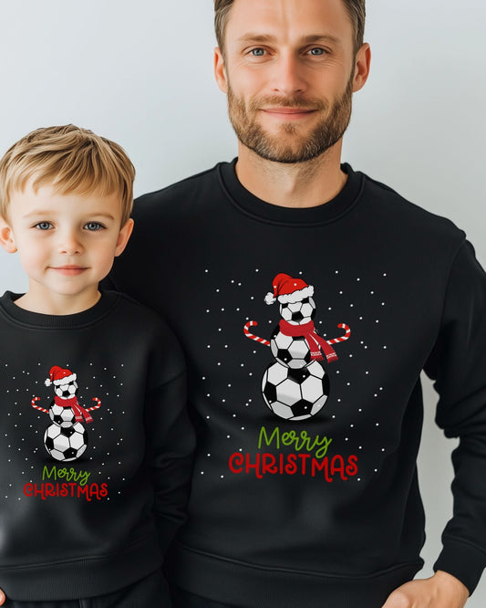 Father and son wearing matching black Christmas sweatshirts featuring a snowman made of footballs with a Santa hat and candy cane arms, perfect for festive football fans.