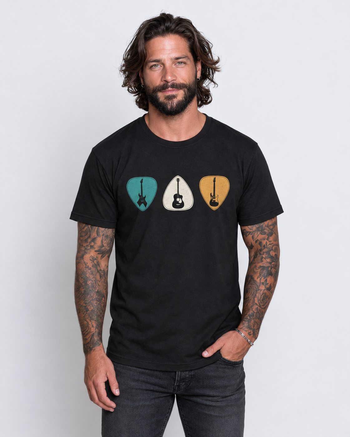 Man with tattooed arms wearing a black T-shirt featuring turquoise, cream and mustard guitar plectrums in a studio.