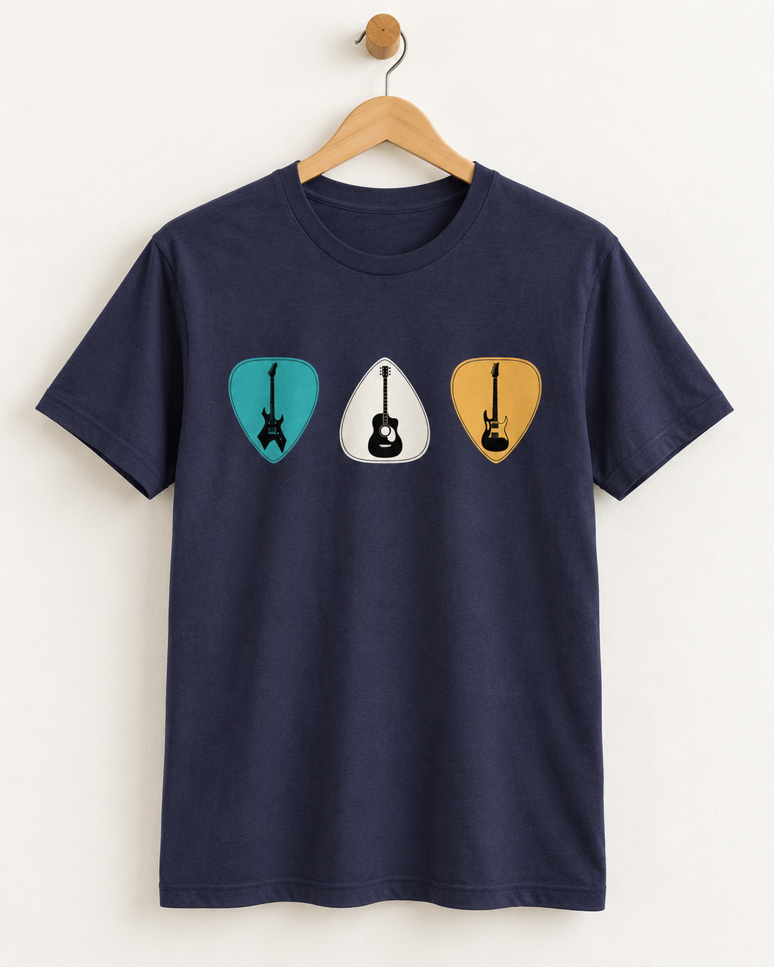 A navy blue short-sleeve t-shirt hanging on a wooden hanger against a plain off-white wall. The shirt features a graphic print of three guitar-shaped picks in teal, white, and mustard yellow on the chest, each containing a black guitar silhouette.