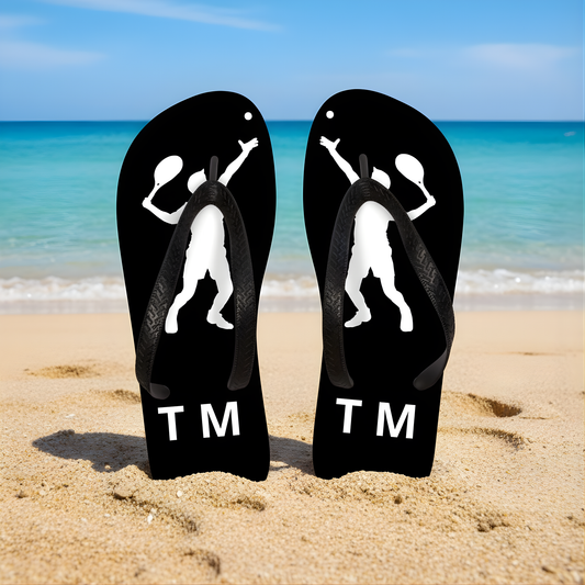 Personalised black tennis flip flops standing on a sandy beach with tennis player silhouette and custom initials.