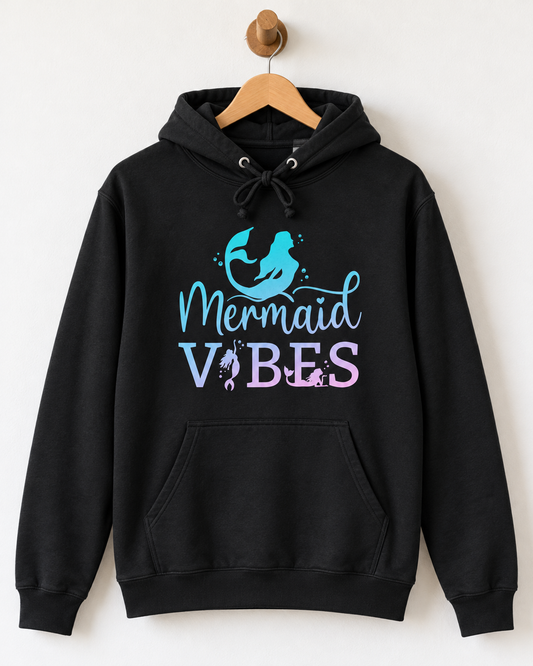 A black pullover hoodie hanging on a wooden hanger against a plain white wall. The hoodie features a graphic on the chest with a blue mermaid silhouette and the text 'Mermaid Vibes' in light blue and lavender-pink lettering.