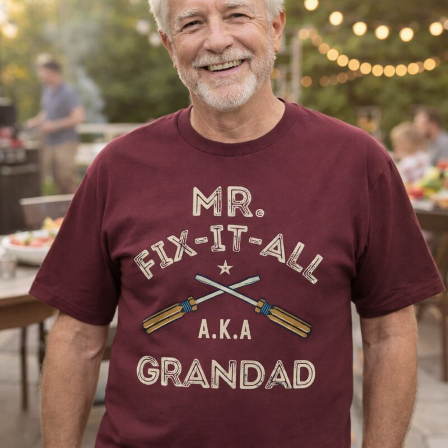 Man wearing a maroon t-shirt with 'Mr. Fix-It-All A.K.A Grandad' text and graphic, standing outdoors.
