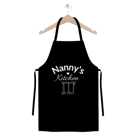 “Nanny’s Kitchen” black cotton twill apron with heart and hanging utensil illustration hanging on a wooden hanger.