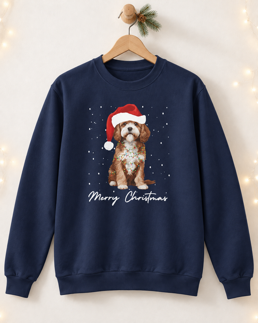 Navy blue Christmas Cavapoo sweatshirt hanging on a wooden hanger against a neutral wall with festive fairy lights background