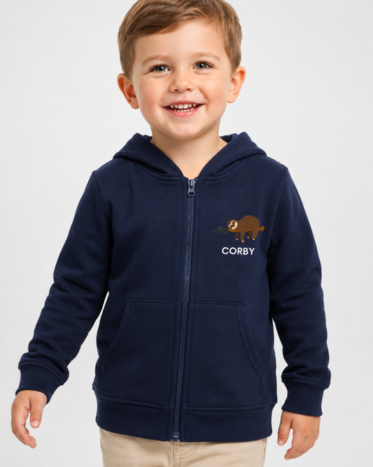Happy young boy wearing a navy personalised kids zip hoodie with a small brown sloth and leafy branch chest design, personalised with the name Corby.