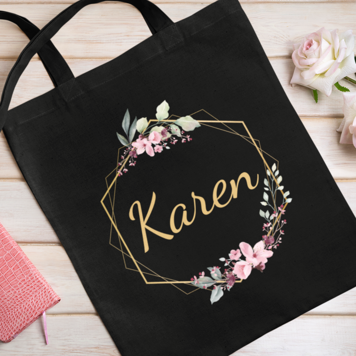 Black tote bag with floral design and 'Karen' text on a wooden surface.