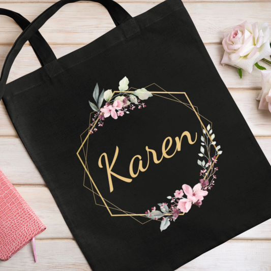 Black tote bag with floral design and 'Karen' text on a wooden surface.