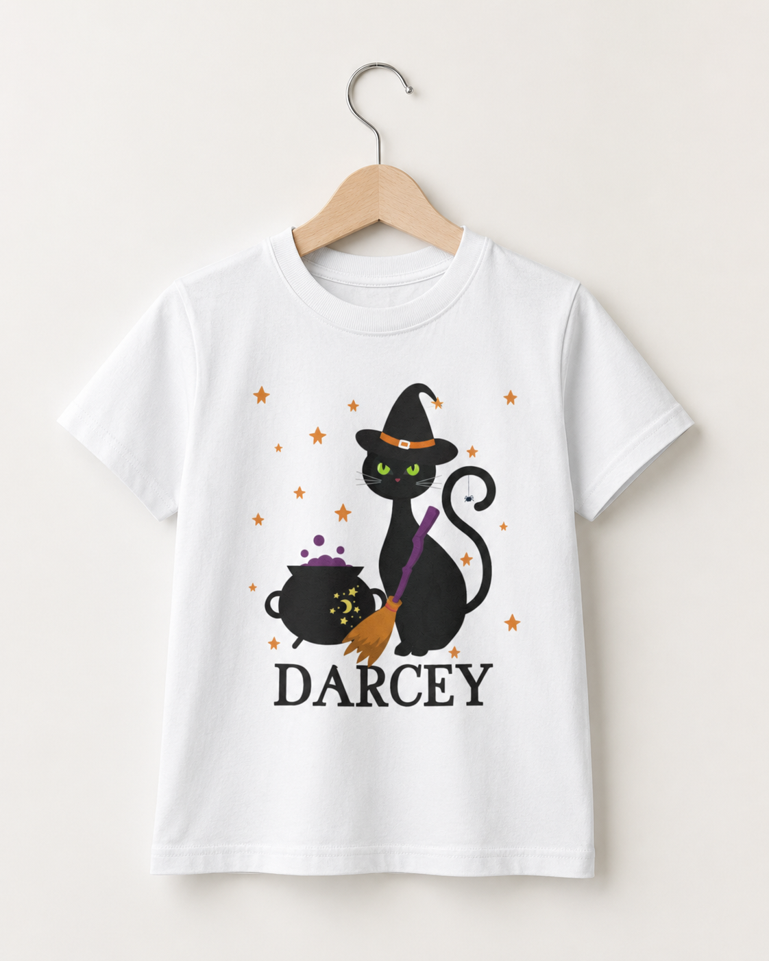 Personalised kids white Halloween T-shirt with black witch cat, bubbling cauldron, broom and the name Darcey, displayed on a wooden hanger.