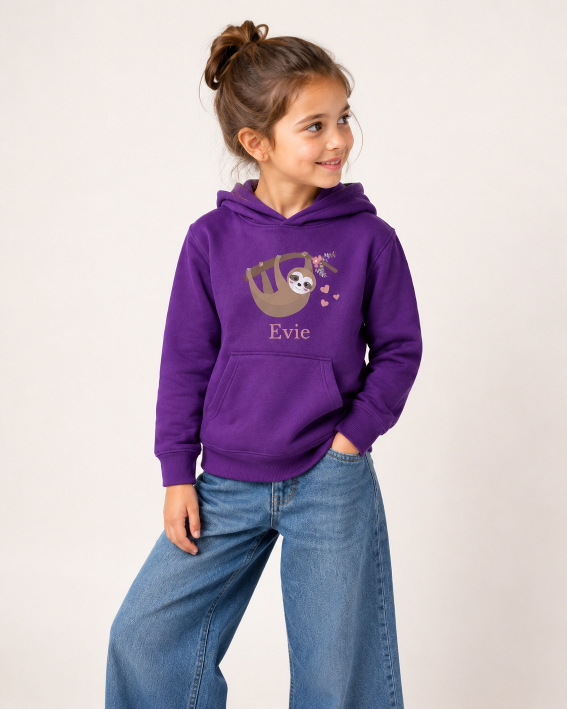 Girl wearing a purple personalised sloth hoodie featuring a smiling sloth hanging from a branch with pink flowers and hearts, with the name Evie printed underneath