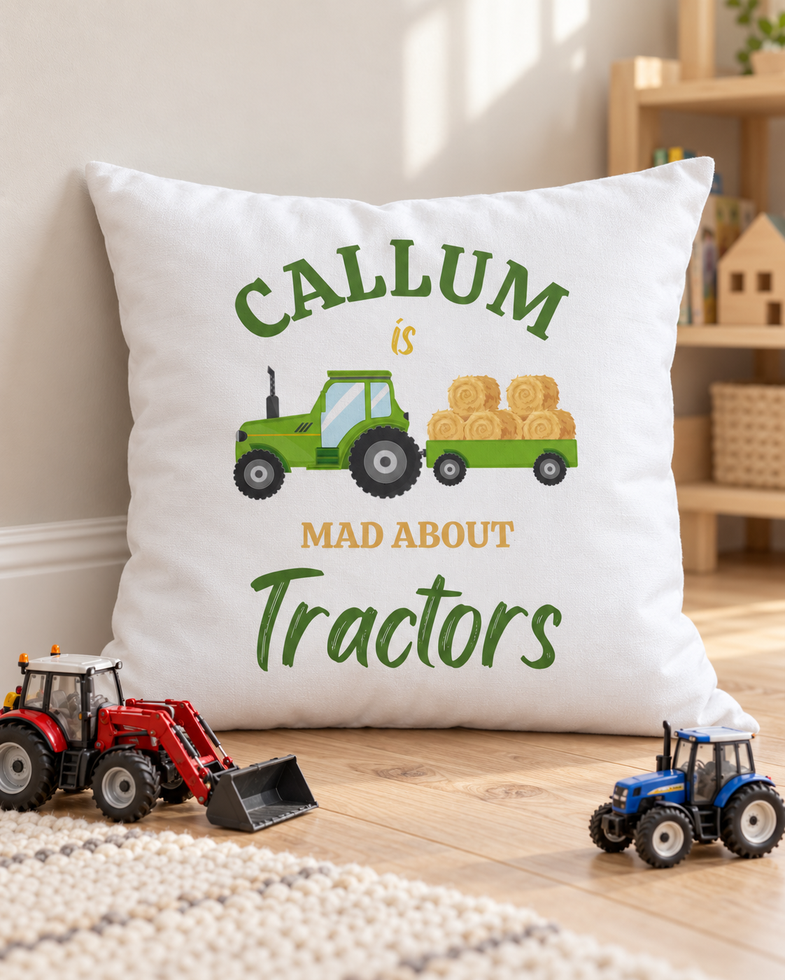 Tractor cushion personalised with Callum, leaning against a playroom wall beside red and blue toy tractors on a wooden floor.