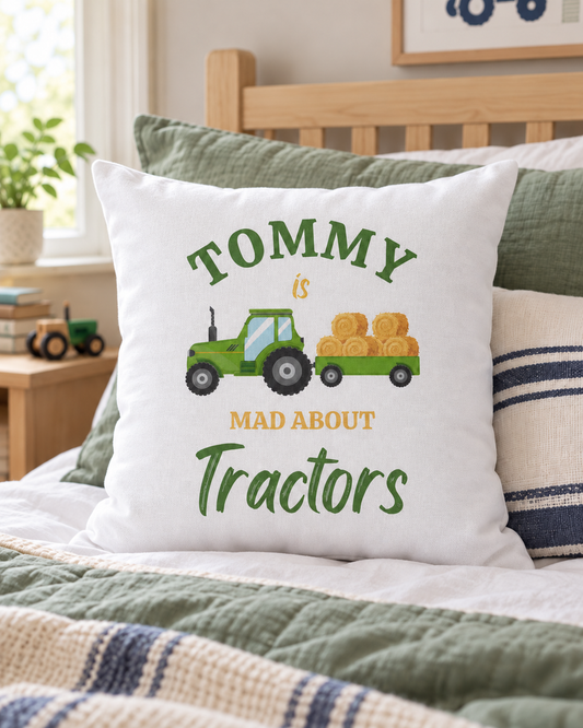 White cushion personalised with Tommy, featuring a green tractor pulling hay bales and “Mad About Tractors” lettering, on a bed with sage bedding.