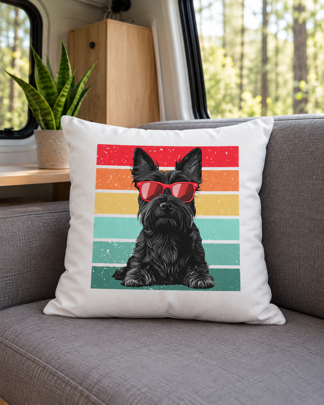 A square white throw cushion resting on a grey fabric seat inside a camper van next to a window. The cushion features a graphic print of a black Scottish Terrier wearing red sunglasses against a retro striped background of red, orange, yellow, teal, and green.