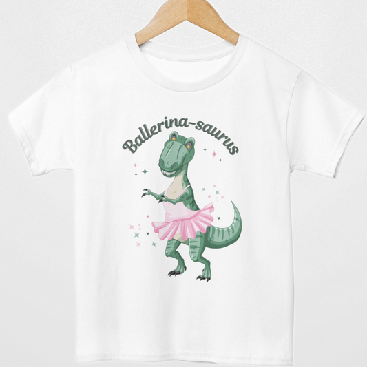 Kids white t-shirt with a dinosaur wearing a pink ballet skirt and 'Ballerina-saurus' arched text, styled on a wooden hanger.