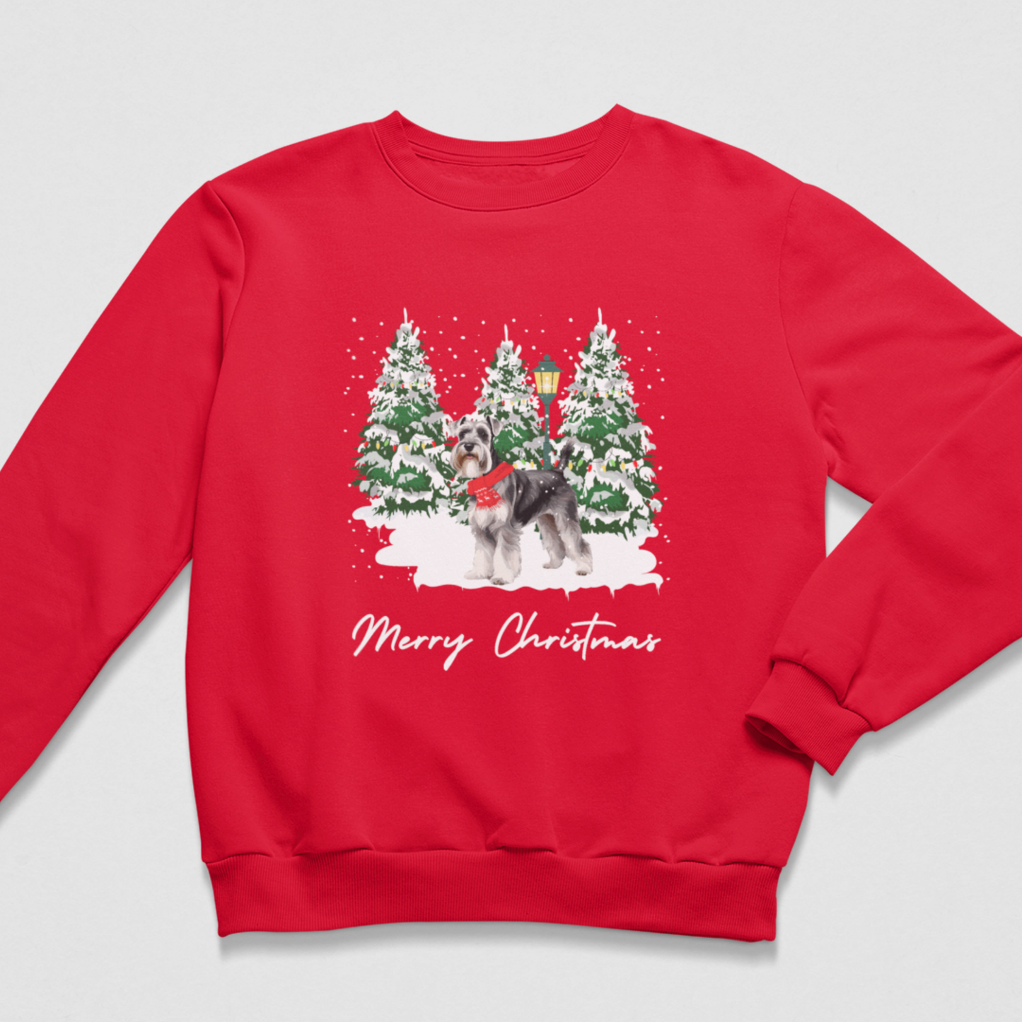 A red crewneck sweatshirt featuring a festive Christmas graphic of a schnauzer in a red scarf standing in front of snow-covered pine trees, with 'Merry Christmas' written in white script below.