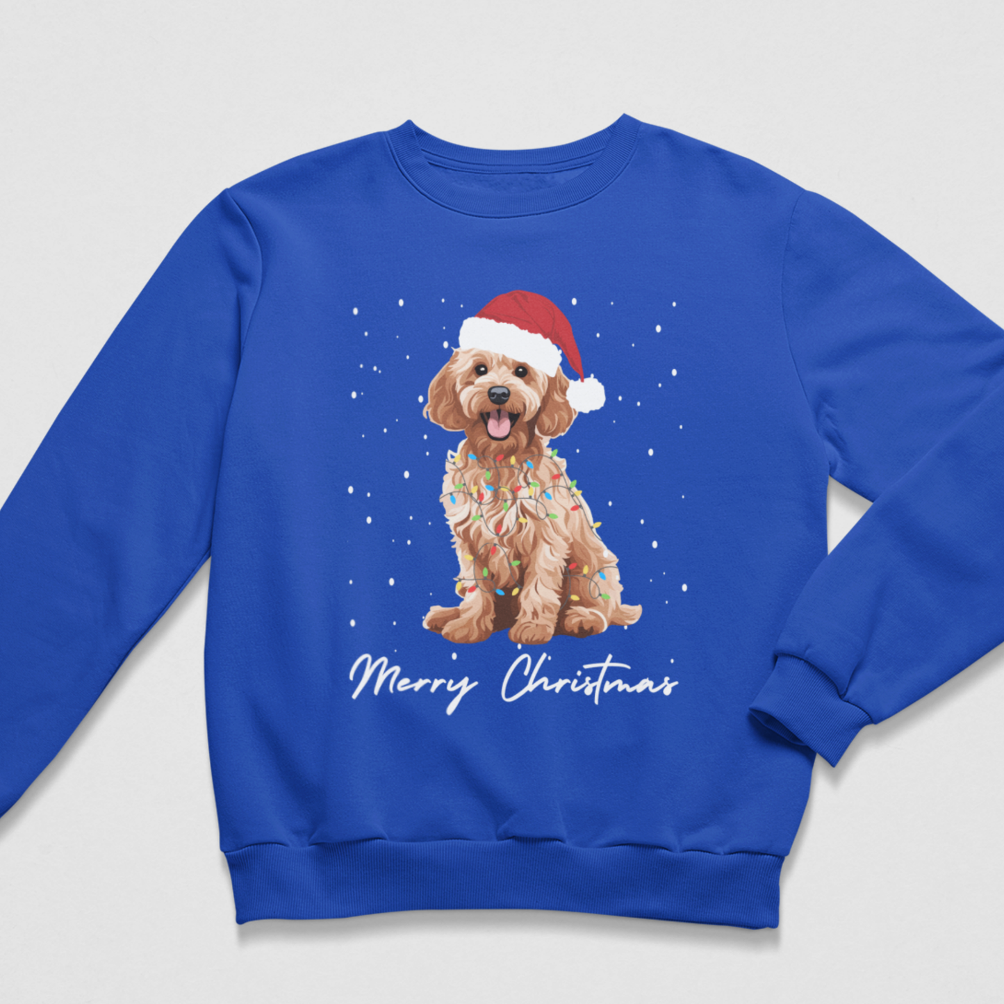 A kids royal blue crewneck sweatshirt featuring a graphic of a golden cockapoo dog wearing a red Santa hat, surrounded by white snowflakes and the text 'Merry Christmas' in white script.