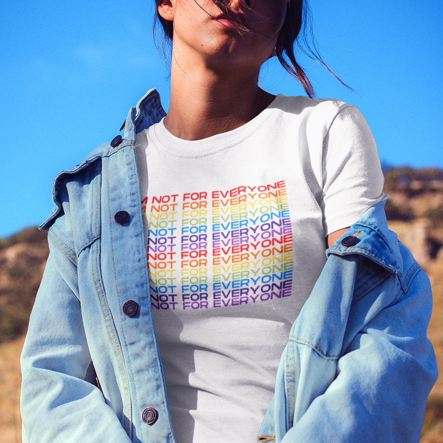 Woman wearing white “I’m Not For Everyone” rainbow slogan t-shirt with denim jacket outdoors
